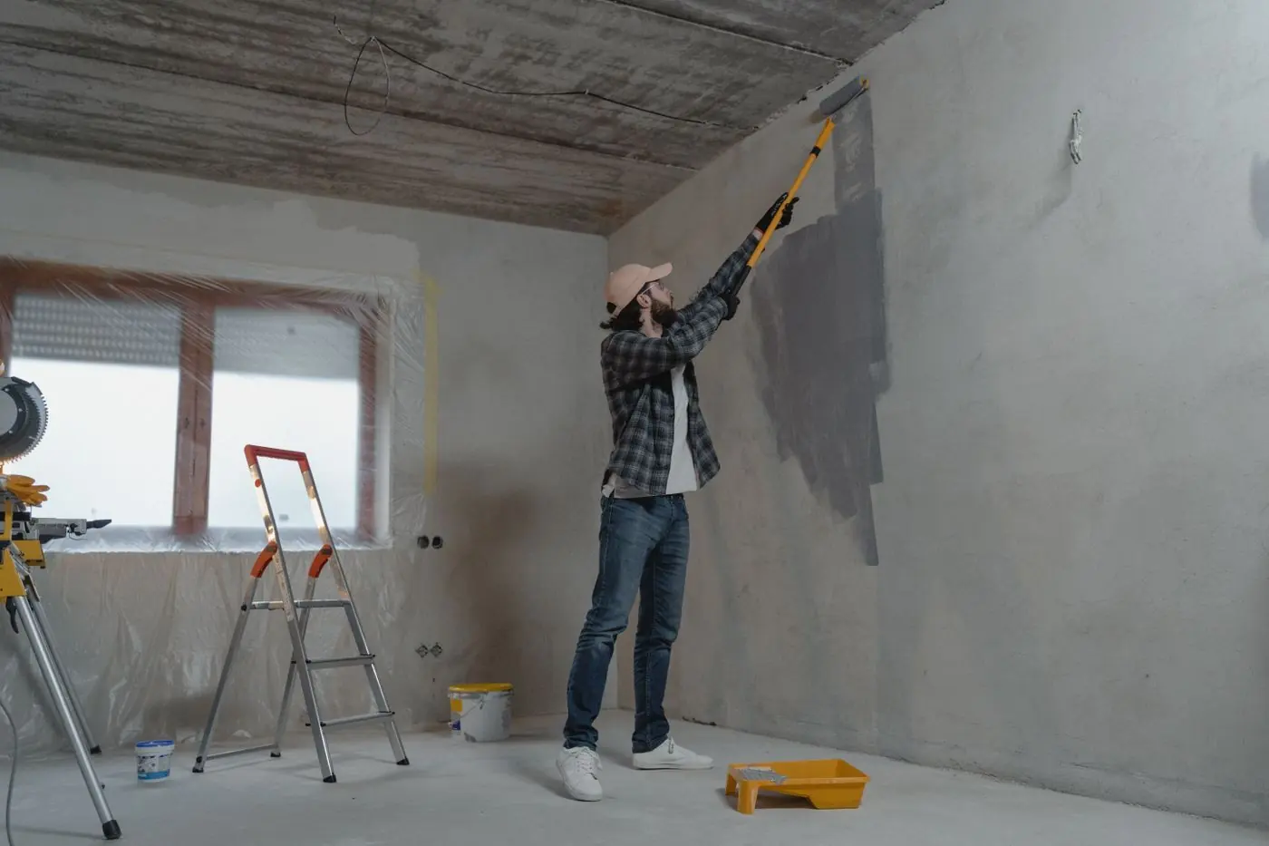 Man verft een grijze muur met een verfroller op een lange steel